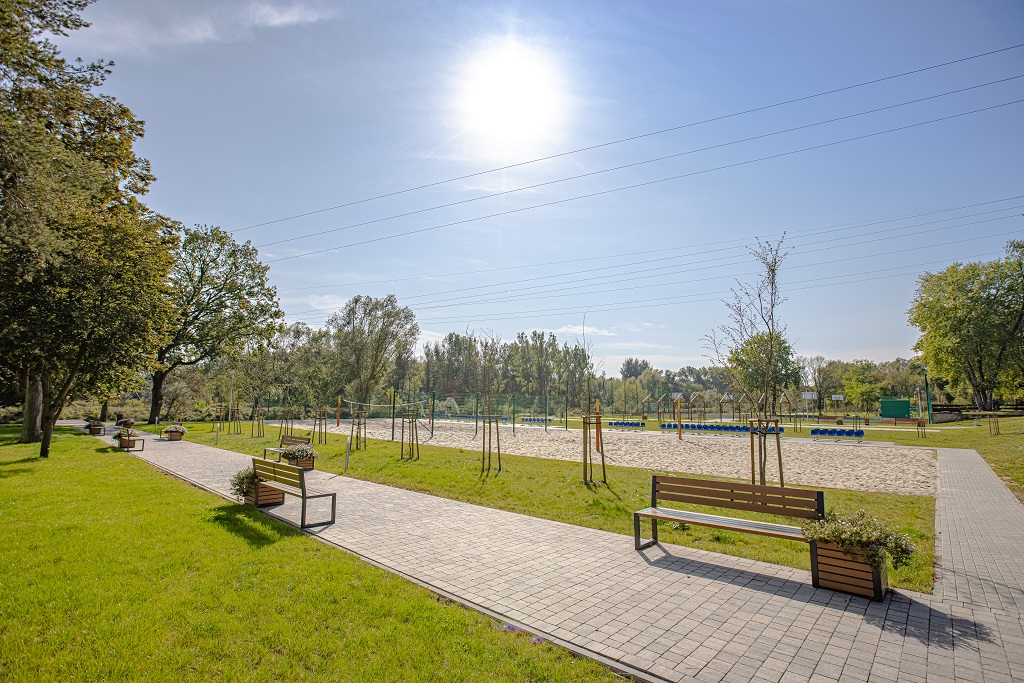 Alt: Widok na ławki, ścieżkę spacerową i boisko do siatkówki plażowej na przystani w Tomaszowie Mazowieckim